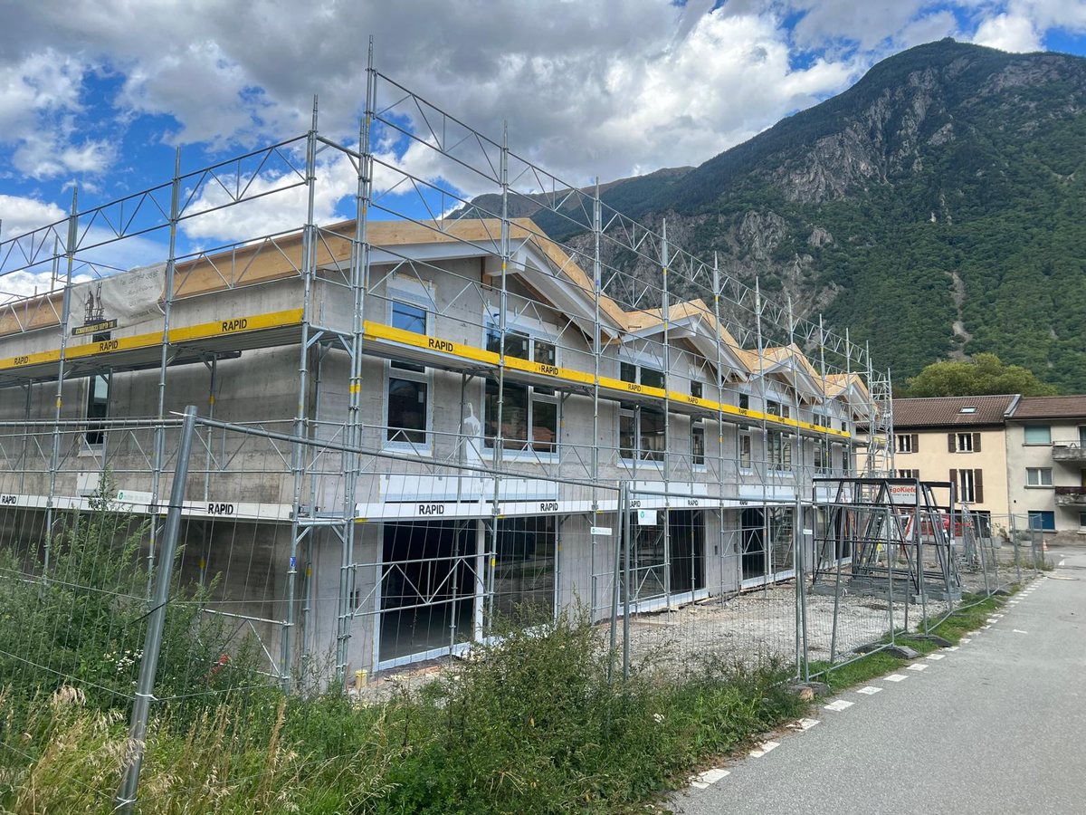 Les maisons de Martigny en construction, sous échafaudage, la charpente posée, au pied de la montagne
