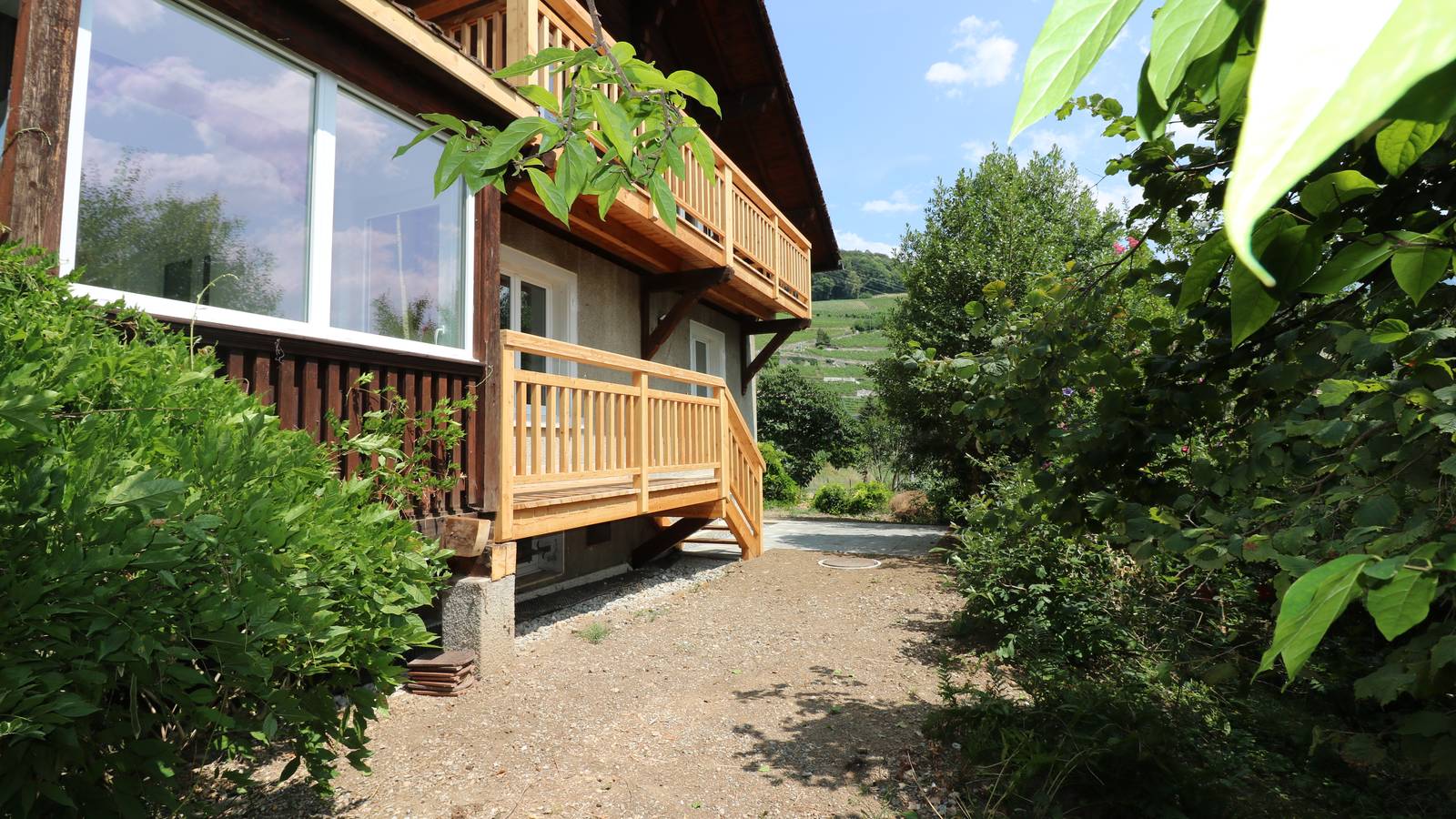 La maison du chemin des Pussines, son balcon de bois clair courant sur la façade, au-dessus du coteau