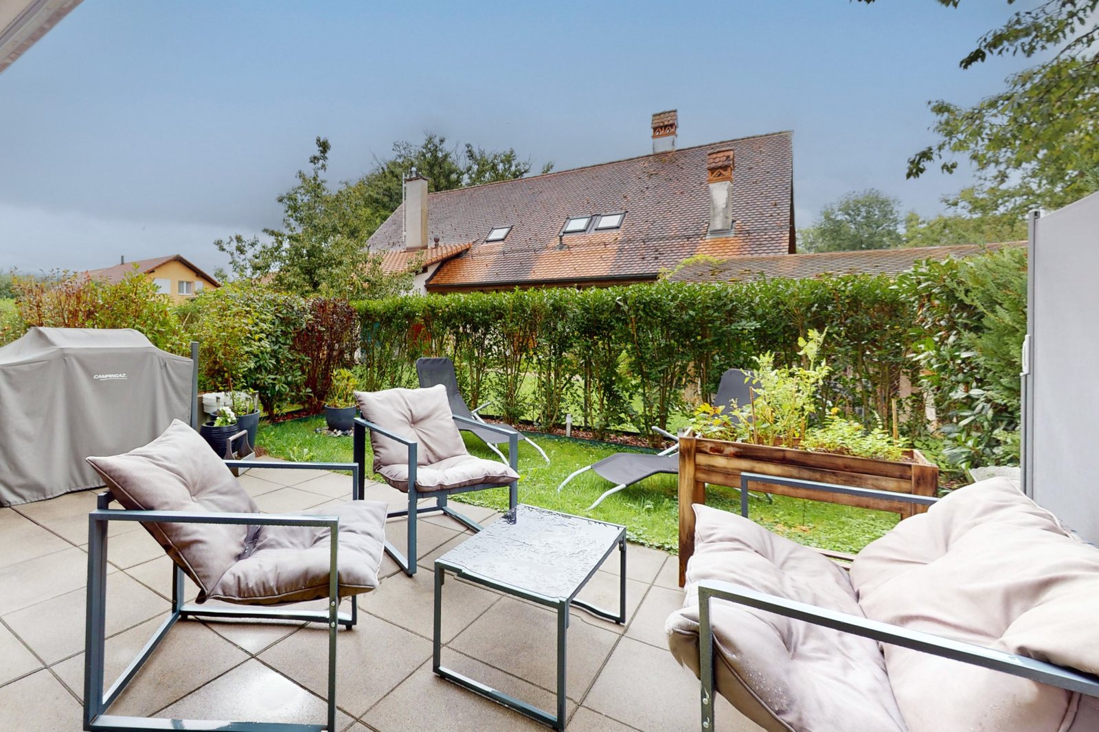 La terrasse dallée d'un appartement du rez, son salon de jardin et sa haie