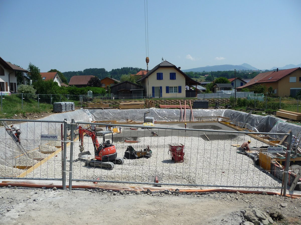 Le terrassement de la Résidence du Château, la fouille clôturée, une pelle mécanique et les maisons du village derrière